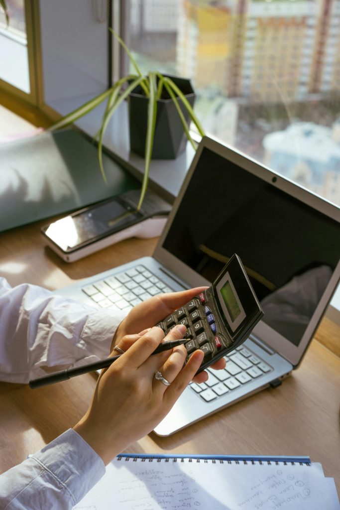 Serviços Person calculating at desk with laptop and notebook. Ideal for business and finance themes.